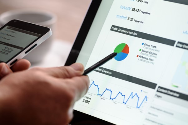 The image shows a person using a pen to point at analytics data displayed on a tablet.